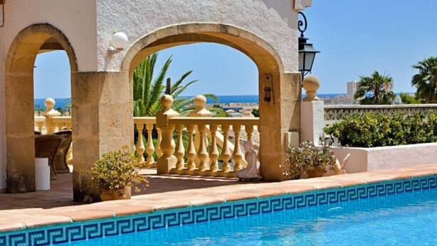 A pool area with a view of the sea, a covered seating area with a balustrade, and a lamp post. - 12 Persoons luxe villa in Javea. Heated pool! (Jávea)