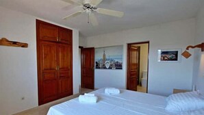 A hotel room with two beds, a ceiling fan, wooden wardrobes, and a cityscape painting on the wall. - 12 Persoons luxe villa in Javea. Heated pool! (Jávea)