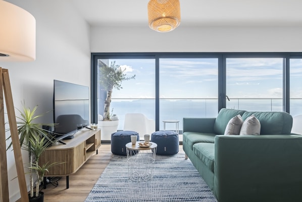 A modern living room with a large window, a flat-screen TV, a green sofa, and a coffee table.