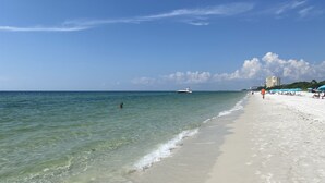 Een strand met helder water, een boot en strandparasols.
