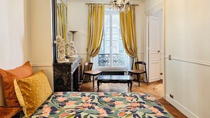 A bedroom with a large bed, a chandelier, a window with curtains, and a door.