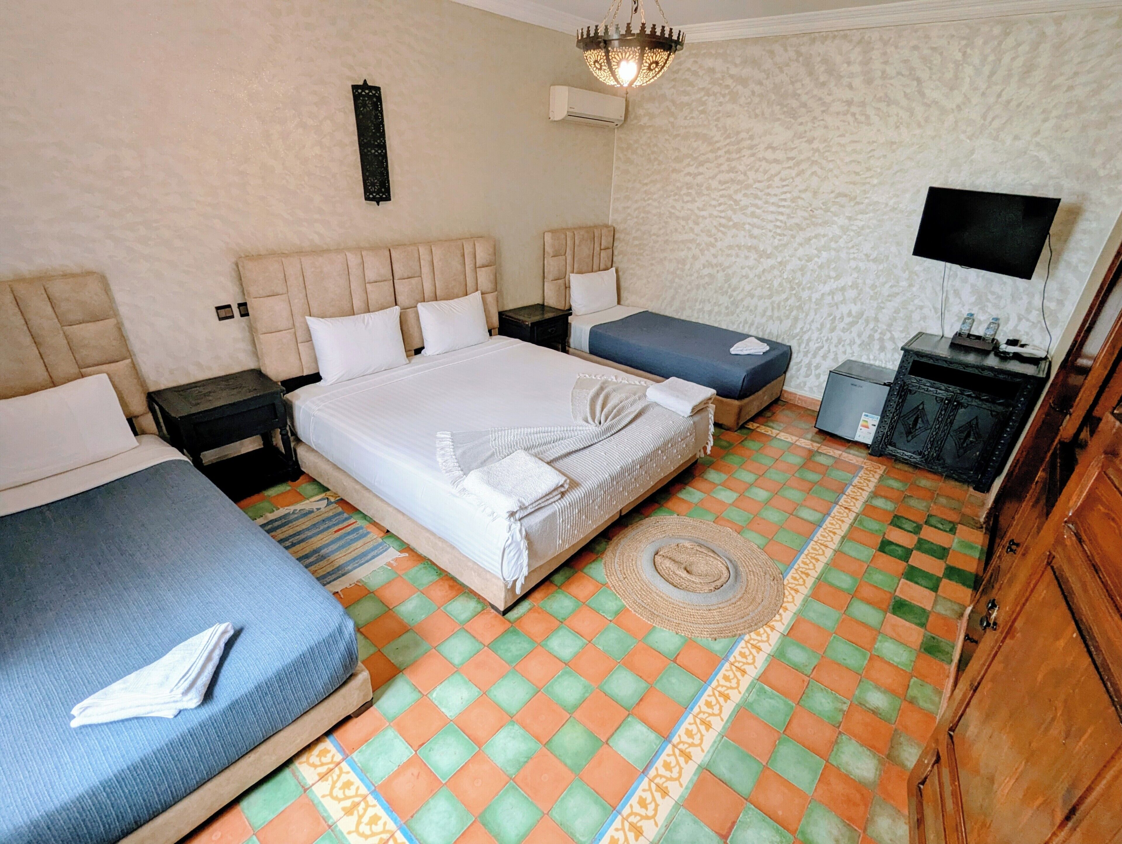 A hotel room with a large bed, two smaller beds, a television, a wardrobe, and a patterned floor.