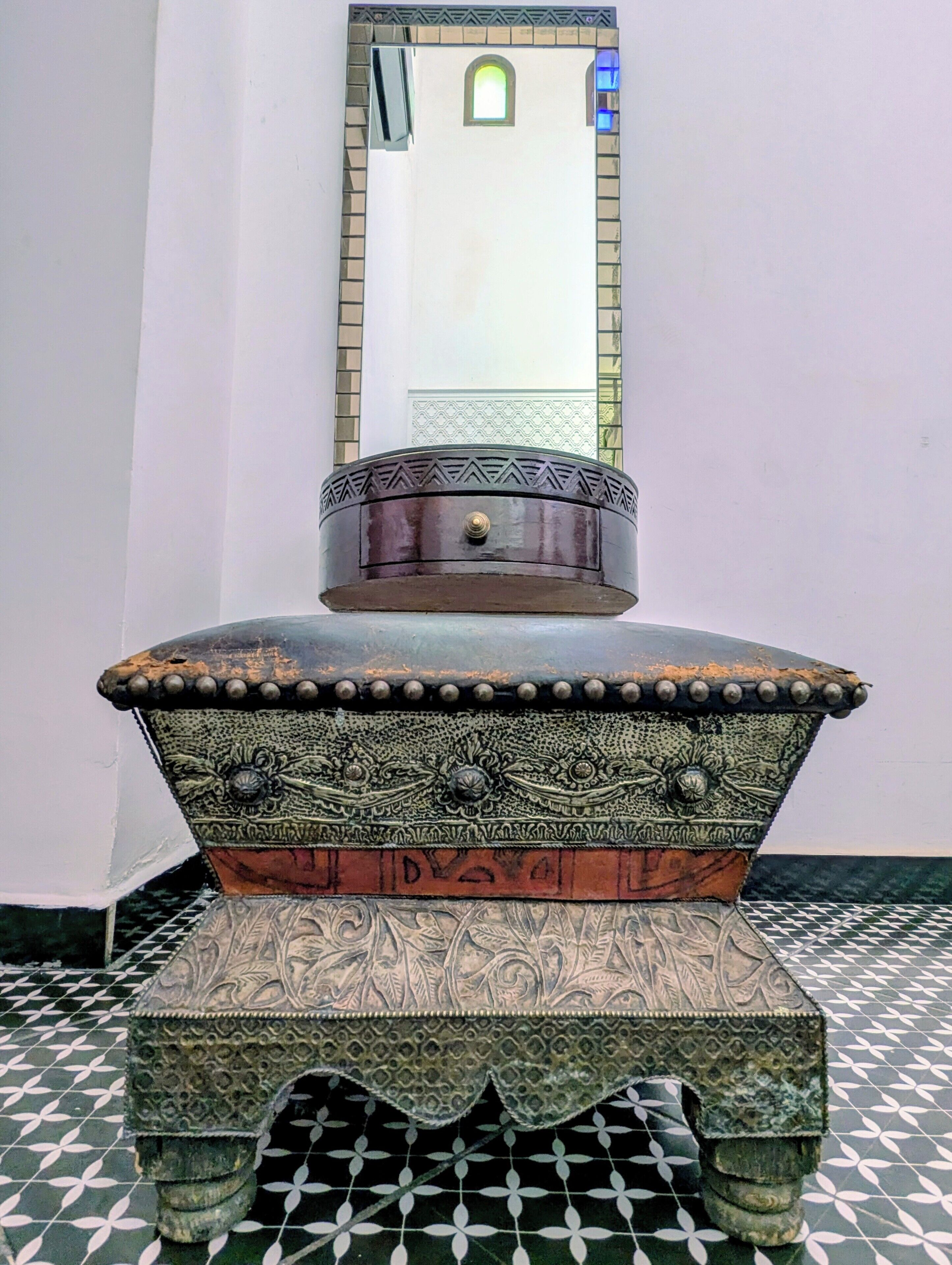 A stone basin with intricate carvings, a mirror above it, and a patterned floor.