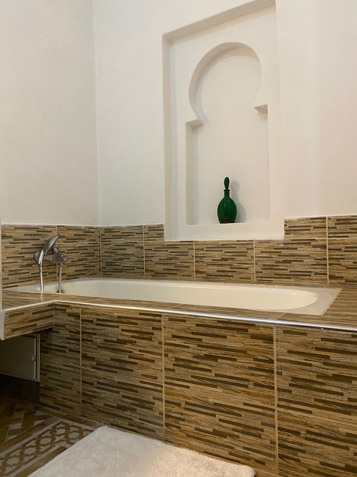 A modern bathroom with a stone-tiled wall, a large bathtub, and a green bottle in a niche.