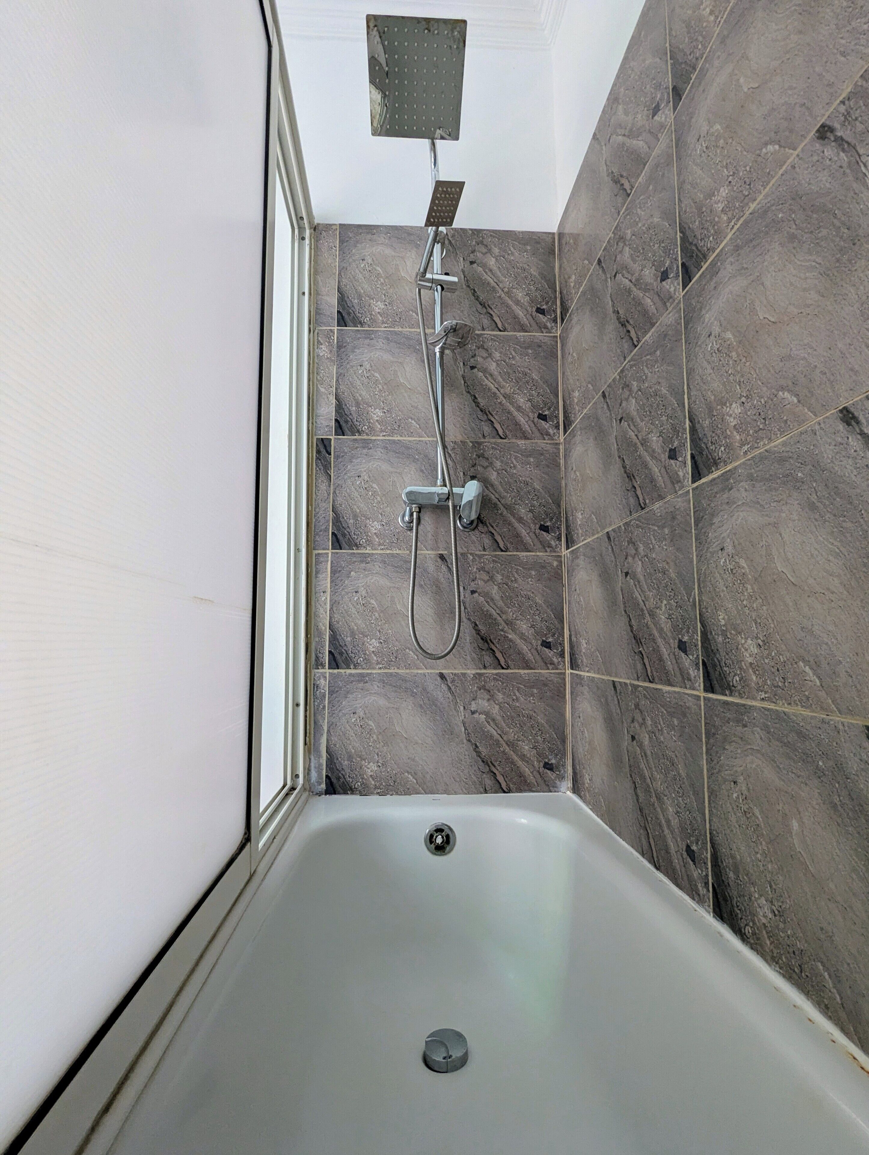 Un baño con ducha, bañera y azulejos de mármol.