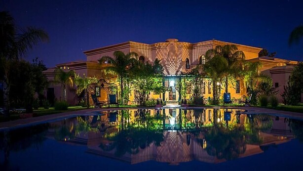 A luxurious hotel with a reflective pool, palm trees, and a well-lit entrance. - Riad Las Palmeras Guest House, Marrakech (Marrakech)