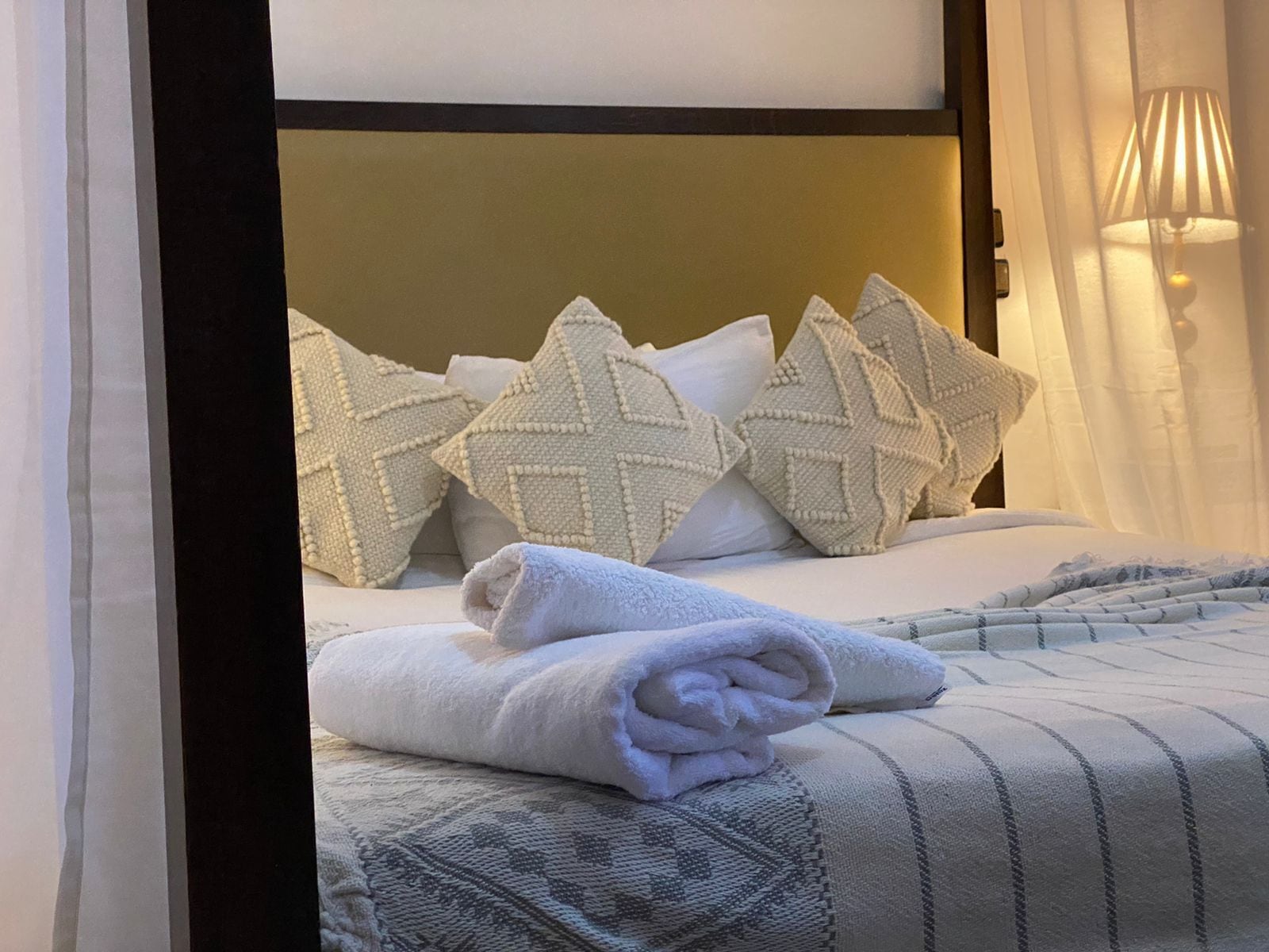 A neatly made bed with a patterned bedspread, a rolled white towel, and decorative pillows.