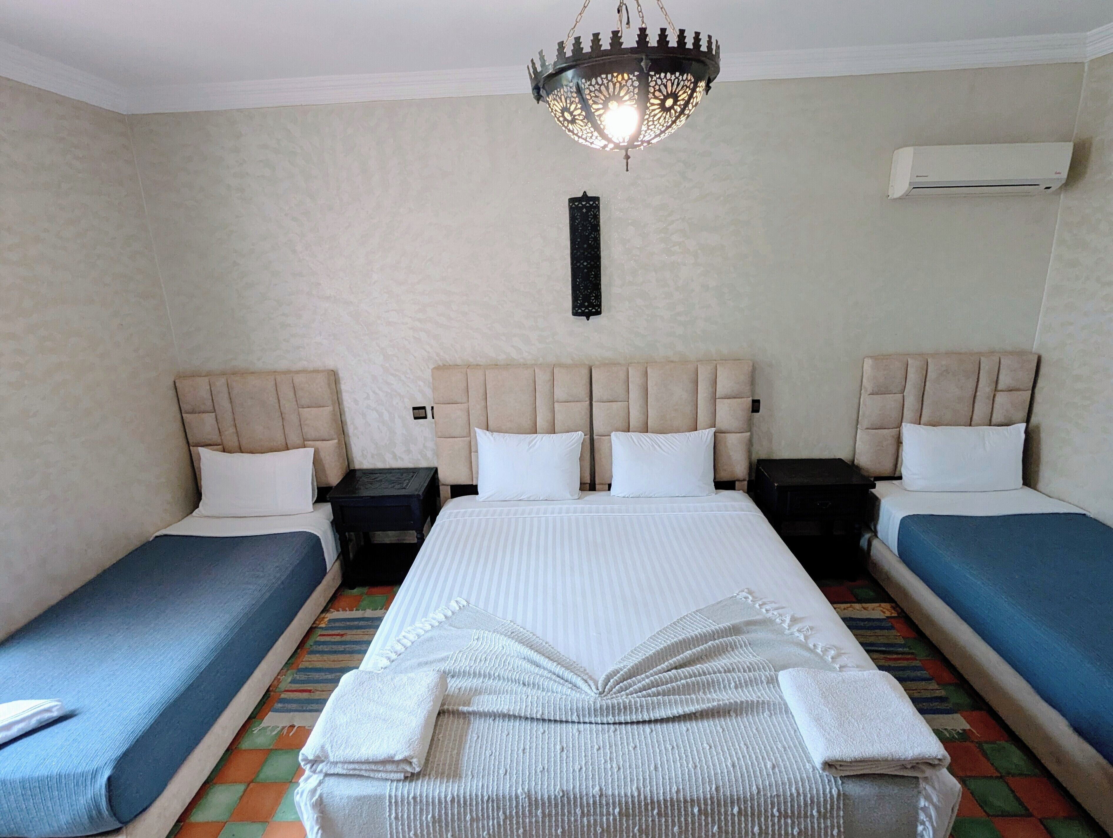 A hotel room with two single beds, a large bed, a chandelier, an air conditioner, and a decorative wall piece.