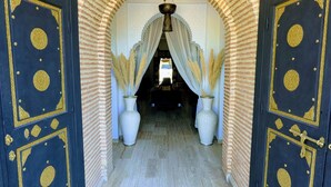 An arched hallway with two large doors, each with gold accents and a patterned design. The floor is tiled, and there are two large vases with tall grasses in the center. - Riad Las Palmeras Guest House, Marrakech (Marrakech)