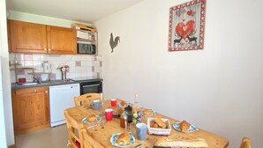 A compact kitchen with wooden cabinets, a microwave, and a sink. A dining table is set with plates, cups, and a bottle. - Haven of peace at the foot of the ski slopes (Le Devoluy)