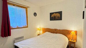 A bedroom with a bed, two bedside lamps, a window with curtains, a wall clock, and a bear-themed picture. - Haven of peace at the foot of the ski slopes (Le Devoluy)