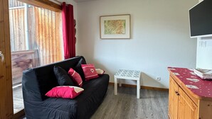 A cozy living area with a black sofa, red cushions, a small white table, and a wooden cabinet. - Haven of peace at the foot of the ski slopes (Le Devoluy)
