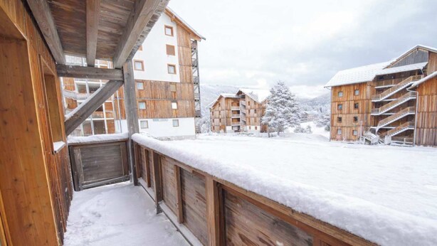 A wooden balcony with snow-covered ground, wooden buildings with balconies, and a snowy landscape. - Haven of peace at the foot of the ski slopes (Le Devoluy)