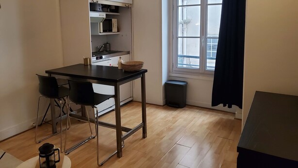 A compact kitchen with a black table, two chairs, a microwave, and a window with curtains.