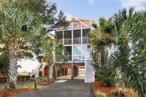 Un hotel a più piani con un ingresso centrale, circondato da palme e un vialetto sterrato.