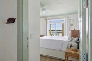 A bedroom with a bed, a window with a view, a ceiling fan, and a bedside table with a lamp.
