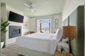 Una camera d'albergo con un letto, una ventola a soffitto, una televisione, una finestra con vista e una pianta.
