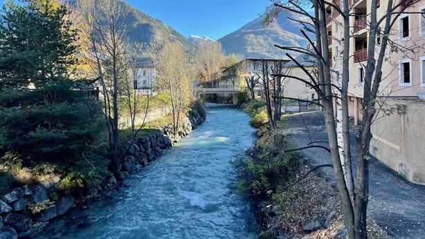 Ein Fluss fließt durch eine Stadt, mit Gebäuden an einer Uferseite und Bergen im Hintergrund.