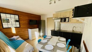 Ein kompakter Wohnraum mit einer Küchenzeile, einem Essbereich mit blauen Stühlen und einem Bett mit blauer Decke.