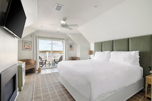 Ein Hotelzimmer mit einem großen Bett, einem Deckenventilator, einem Fernseher, einem Schreibtisch, einem Sessel und einem Balkon mit Blick.