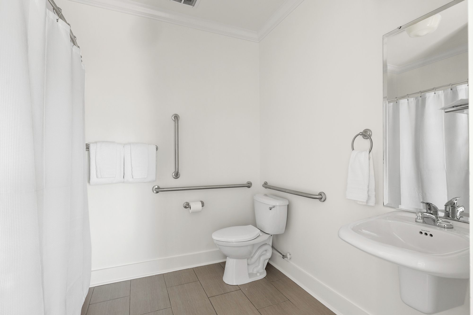 A bathroom with a toilet, a sink, a shower curtain, and grab bars.