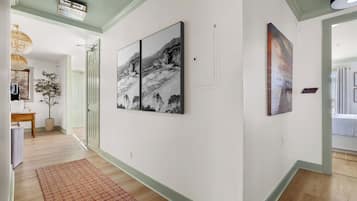 A hallway with artwork on the walls, a wooden floor, and a door leading to another room.