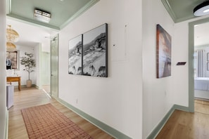 Un passadís amb obres d'art a les parets, un terra de fusta i una porta que condueix a una altra habitació.