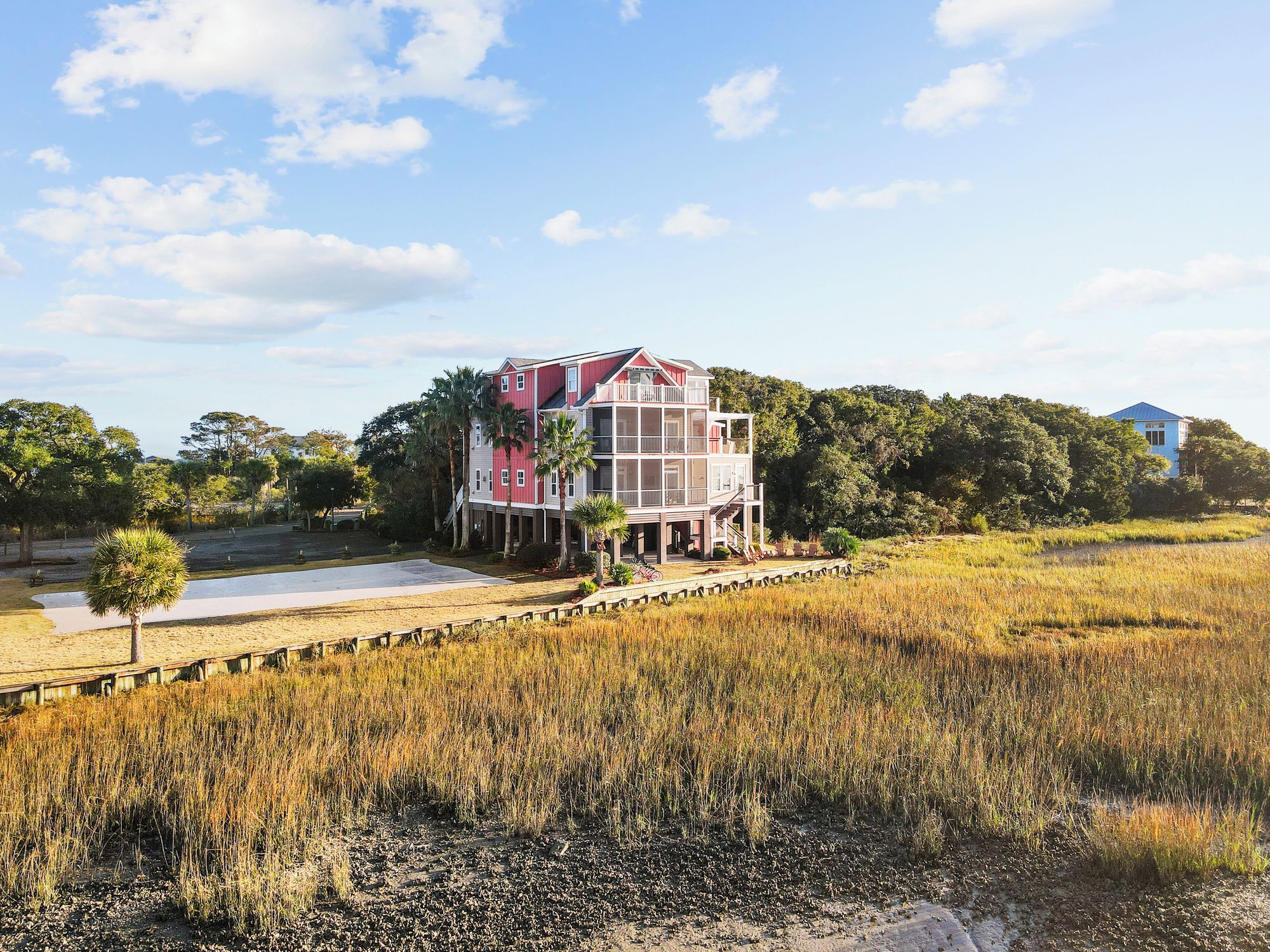 A two-story house with a balcony, surrounded by a natural landscape with trees and a field.