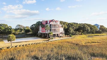 A two-story house with a balcony, surrounded by a natural landscape with trees and a field.
