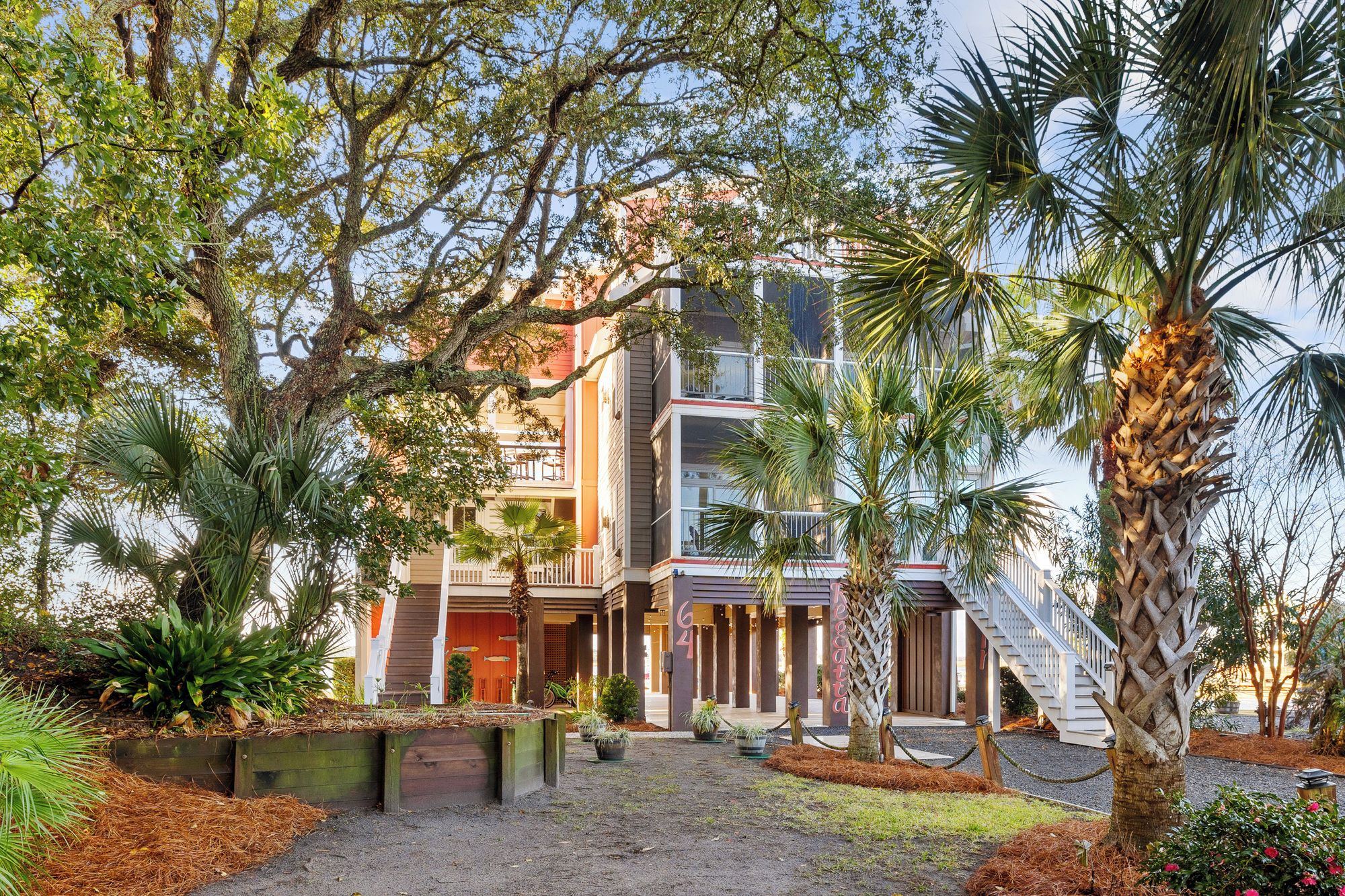 A two-story building with a balcony, surrounded by various plants and trees.