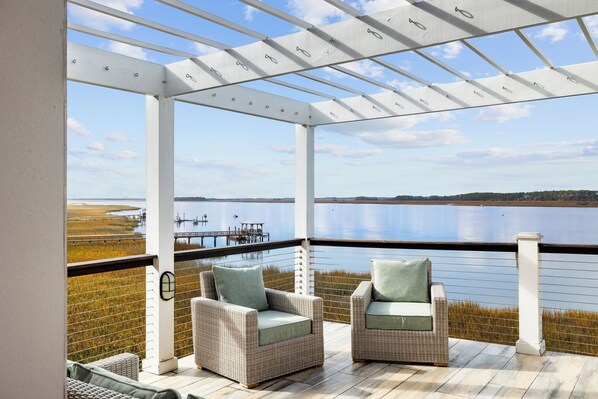 A covered outdoor seating area with two wicker chairs and a view of a calm lake.