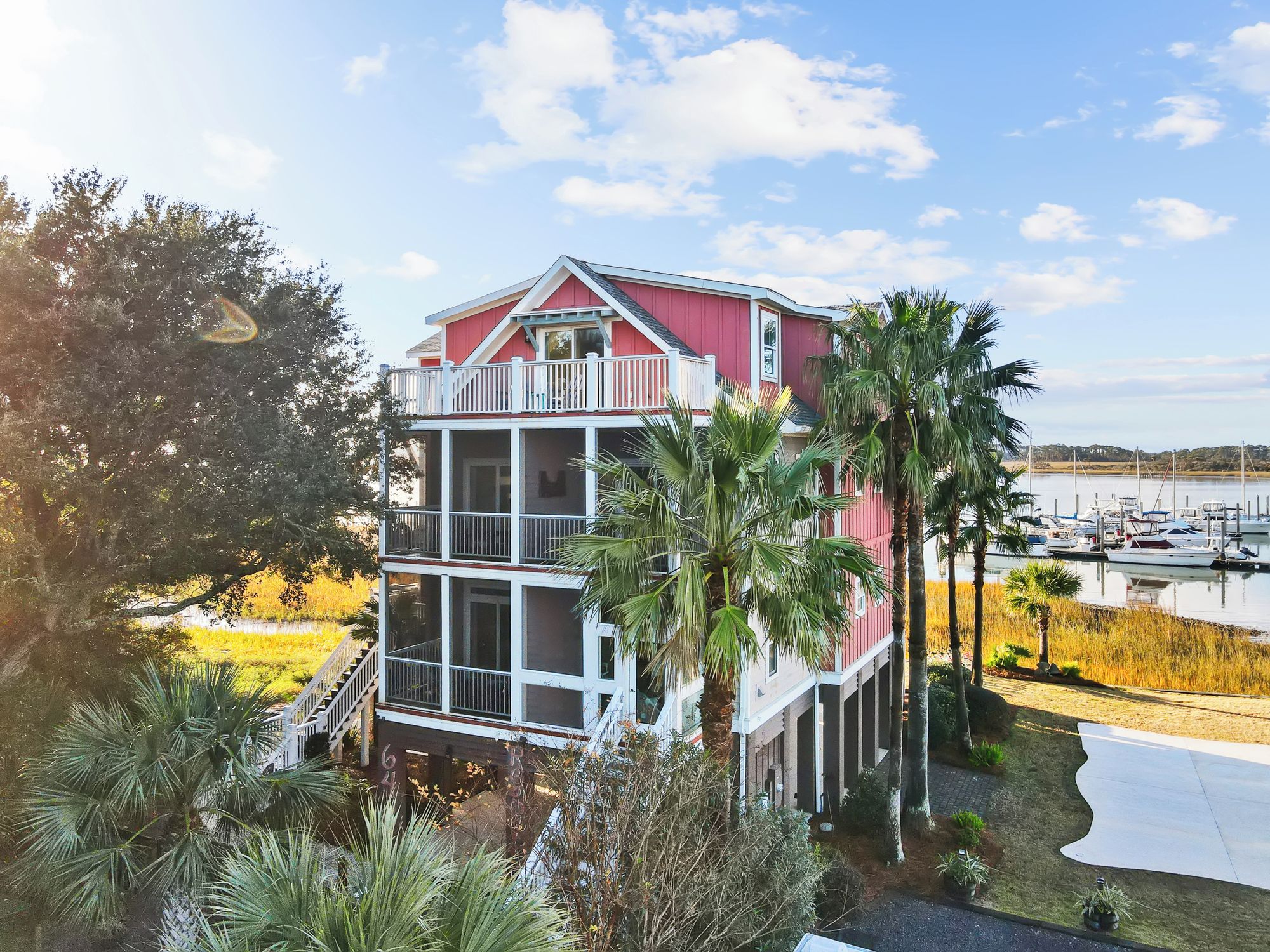 A multi-story building with a balcony, surrounded by palm trees and a body of water with boats.