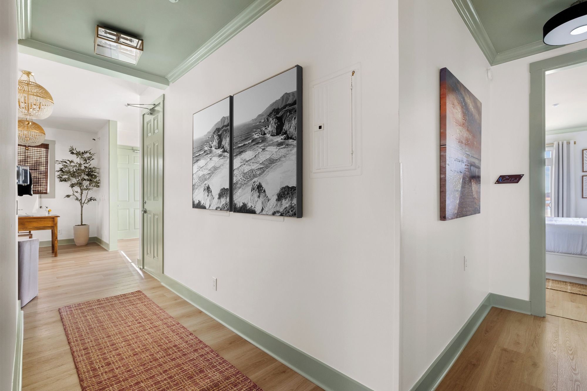 A hallway with artwork on the walls, a wooden floor, and a door leading to another room.