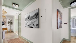 Un pasillo con obras de arte en las paredes, piso de madera y una puerta que da a otra habitación.