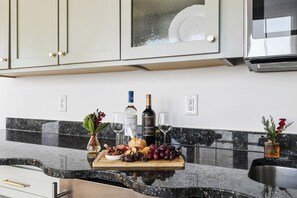 A kitchen counter with a marble backsplash, a wine bottle, a glass, and a wooden board with food items.