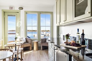 Una cucina con vista sul porto turistico, una zona pranzo con sedie e tavolo, e un bancone con bottiglie di vino e bicchieri.