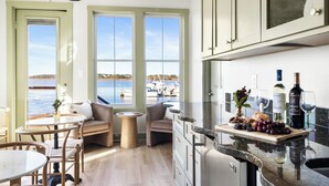 Una cocina con vista al puerto deportivo, un comedor con sillas y mesa, y una encimera con botellas de vino y copas.