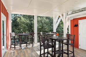 Eine Terrasse im Freien mit Holztischen und -stühlen, umgeben von einer weißen Struktur mit Glasüren.