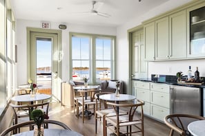 Una stanza con vista sul porto turistico, un'area pranzo con tavoli e sedie rotonde e una cucina con mobili color verde chiaro.