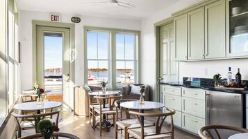 Ein Zimmer mit Blick auf die Marina, ein Essbereich mit runden Tischen und Stühlen sowie eine Küche mit hellgrünen Schränken.