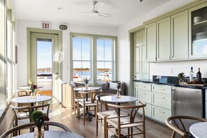 Ein Zimmer mit Blick auf die Marina, ein Essbereich mit runden Tischen und Stühlen sowie eine Küche mit hellgrünen Schränken.