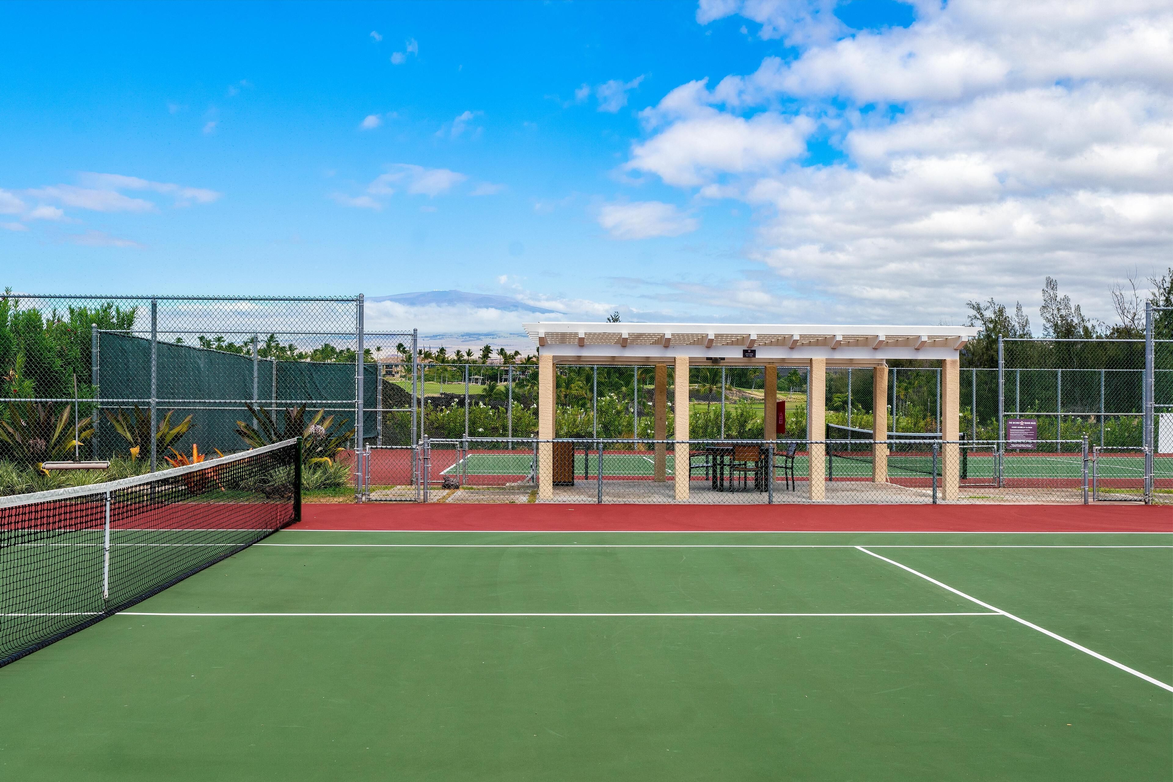 A tennis court with a net, a covered seating area, and a fence.