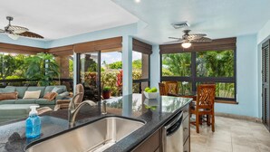Una cocina moderna con encimera negra, pileta de acero inoxidable y un rincón comedor con una silla y mesa de madera.