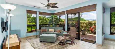 A spacious room with a large window, a ceiling fan, a sofa, a chair, and a small table.