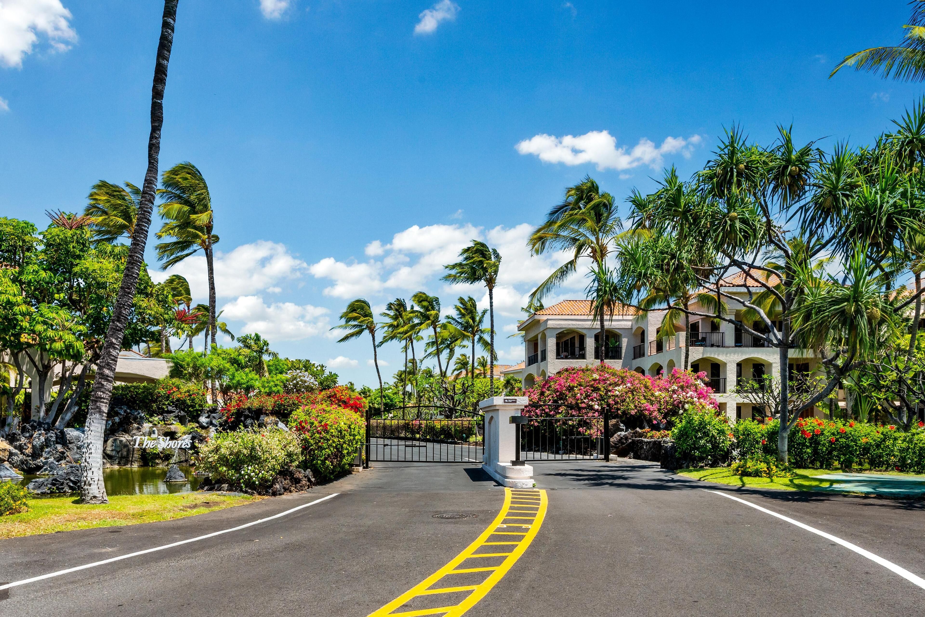 A hotel entrance with a paved driveway, palm trees, and a building with a tiled roof.