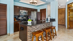 Una cocina moderna con armarios de madera oscura, electrodomésticos de acero inoxidable, encimera negra y salpicadero azulejado.