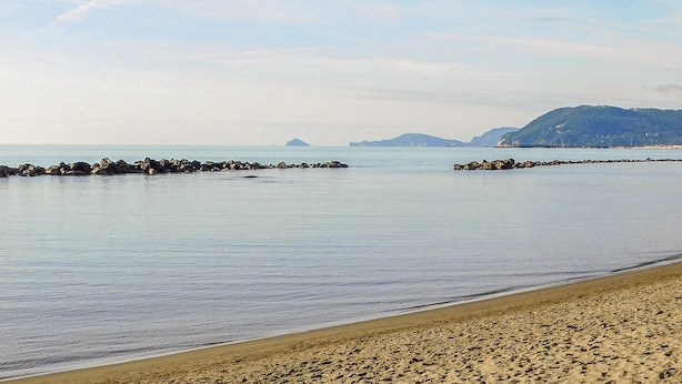 A beach with calm waters, a rocky breakwater, and distant hills. - Casale Il Farro (Camaiore)