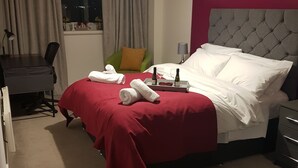 Een hotelkamer met een bed, een bureau, een stoel, een raam met gordijnen en een schilderij aan de muur.