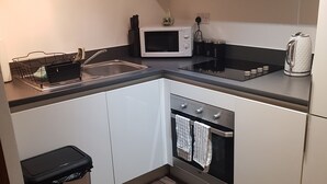 Een kleine keuken met een magnetron, spoelbak, waterkoker en oven.