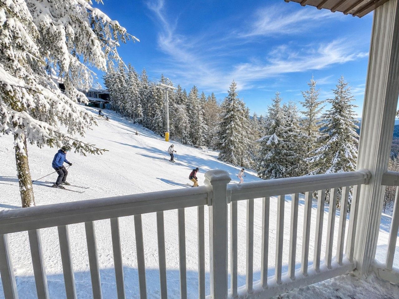 Une piste de ski enneigée avec des skieurs, une clôture en bois et des arbres couverts de neige.